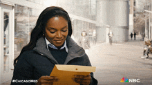 a woman holding a piece of paper with the nbc logo on the bottom right