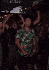 a man in a green hawaiian shirt is dancing in a crowd .