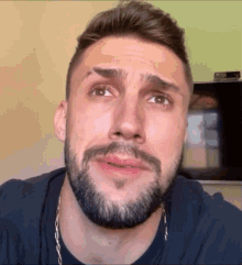 a man with a beard wearing a chain around his neck looks at the camera