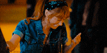 a woman wearing a bandana and a denim jacket is smiling and looking at her phone