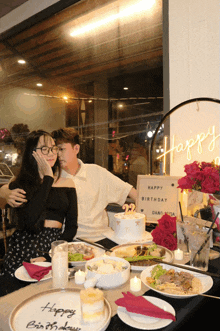 a man and woman are sitting at a table with plates of food and a sign that says happy birthday on it