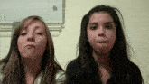 two young girls are making funny faces in front of a white wall .