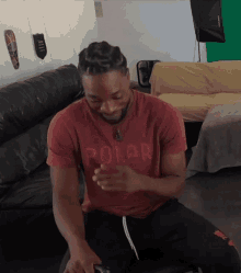 a man wearing a red polar t-shirt is sitting on a couch