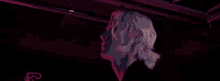 a young man with blonde hair is standing in a dark room with red lights .