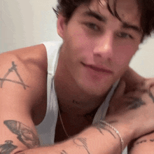 a man with a lot of tattoos on his arms and chest is wearing a white tank top and a necklace .