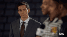 a man in a suit and tie is talking to another man in a bet logo shirt