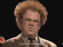 a man with curly hair and glasses is wearing a suit and tie and talking .