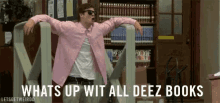a man in a pink shirt and sunglasses is standing in front of a bookshelf in a library .