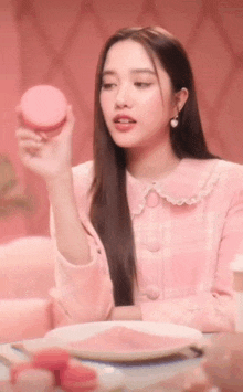a woman in a pink dress is holding a pink macaroon in her hand .