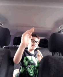 a boy wearing glasses and a hulk shirt is giving the middle finger