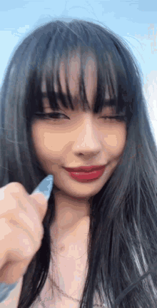 a woman with long black hair and red lipstick is holding a marker in her hand .