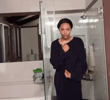 a woman in a black dress is standing in a bathroom next to a shower .