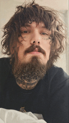 a man with curly hair and a beard has a tattoo on his forehead