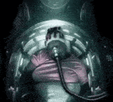a man in a pink shirt is sitting in an oxygen chamber .