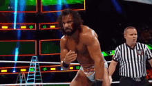 a man with a beard is standing in a wrestling ring while a referee watches .