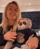 a woman holds a stuffed sloth wearing a black shirt that says copinha