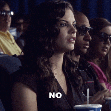 a woman sitting in a theater with a cup of soda and the word no on her face