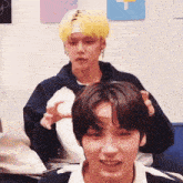 two young men are sitting next to each other in a room and one of them is holding the other 's head .