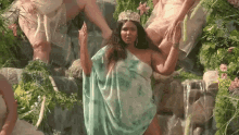 a woman wearing a crown is standing in front of a waterfall .