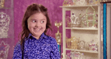 a little girl is making a funny face in front of a shelf filled with tiaras .