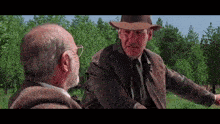 a man in a hat and leather jacket is talking to another man