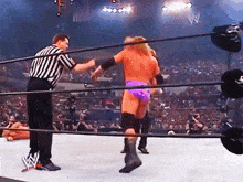 a wrestler in a purple shorts is standing in the middle of a wrestling ring with a referee