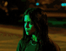 a woman with long dark hair is wearing a green shirt and a chain around her neck