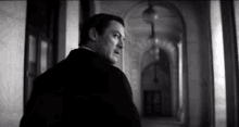 a black and white photo of a man standing in a hallway with arches .