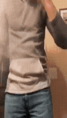 a man in a gray shirt and blue jeans is taking a selfie in a bathroom .