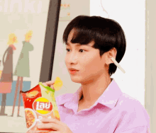 a man in a purple shirt is eating a bag of lays potato chips