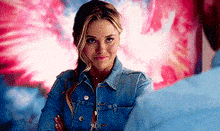 a woman in a denim jacket is standing in front of a man with her arms crossed .