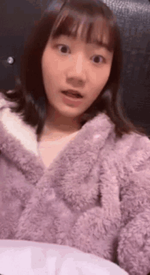 the girl is wearing a purple furry jacket and making a surprised face .