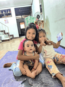 a girl holding a baby and another girl holding a cell phone are sitting on a blue mat