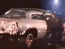 a man is standing next to a car that has graffiti on the side