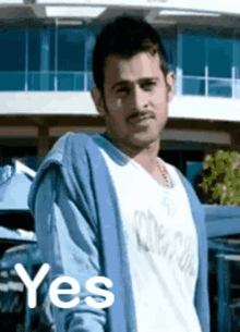 a man wearing a blue cardigan and a white shirt is standing in front of a building and says yes