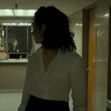 a woman in a white shirt and black skirt stands in a hallway