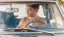 a shirtless man is driving a car with his eyes closed
