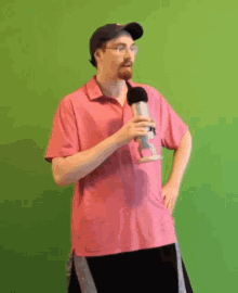 a man in a pink shirt holds a microphone in front of a green background