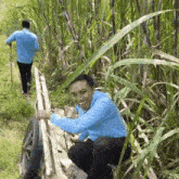 a man in a blue shirt is pushing a wooden cart through a grassy field