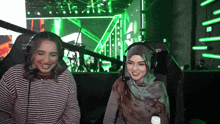 two women wearing headphones are sitting in front of a green screen that says team of