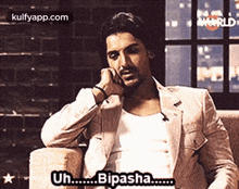 a man in a suit is sitting on a couch with his hand on his chin and says bipasha .
