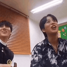 two young men are sitting next to each other in a room laughing .