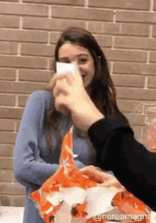 a woman covering her face with a piece of paper while a person holds a bag of chips