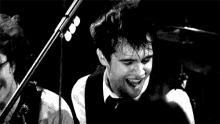a black and white photo of a man playing a guitar in front of a microphone on a stage .