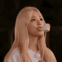 a woman with long blonde hair is eating a marshmallow on a stick .