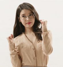 a woman wearing glasses and a tan sweater holds her hair