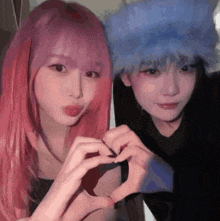 two girls with pink hair and blue hair are making a heart shape with their hands .