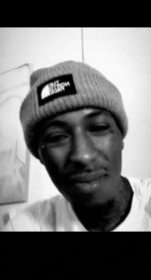 a black and white photo of a man wearing a beanie and a white shirt .