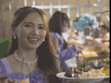 a woman in a purple dress is holding a plate of food and smiling at the camera .