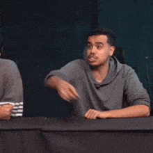 a man is sitting at a table and pointing his finger